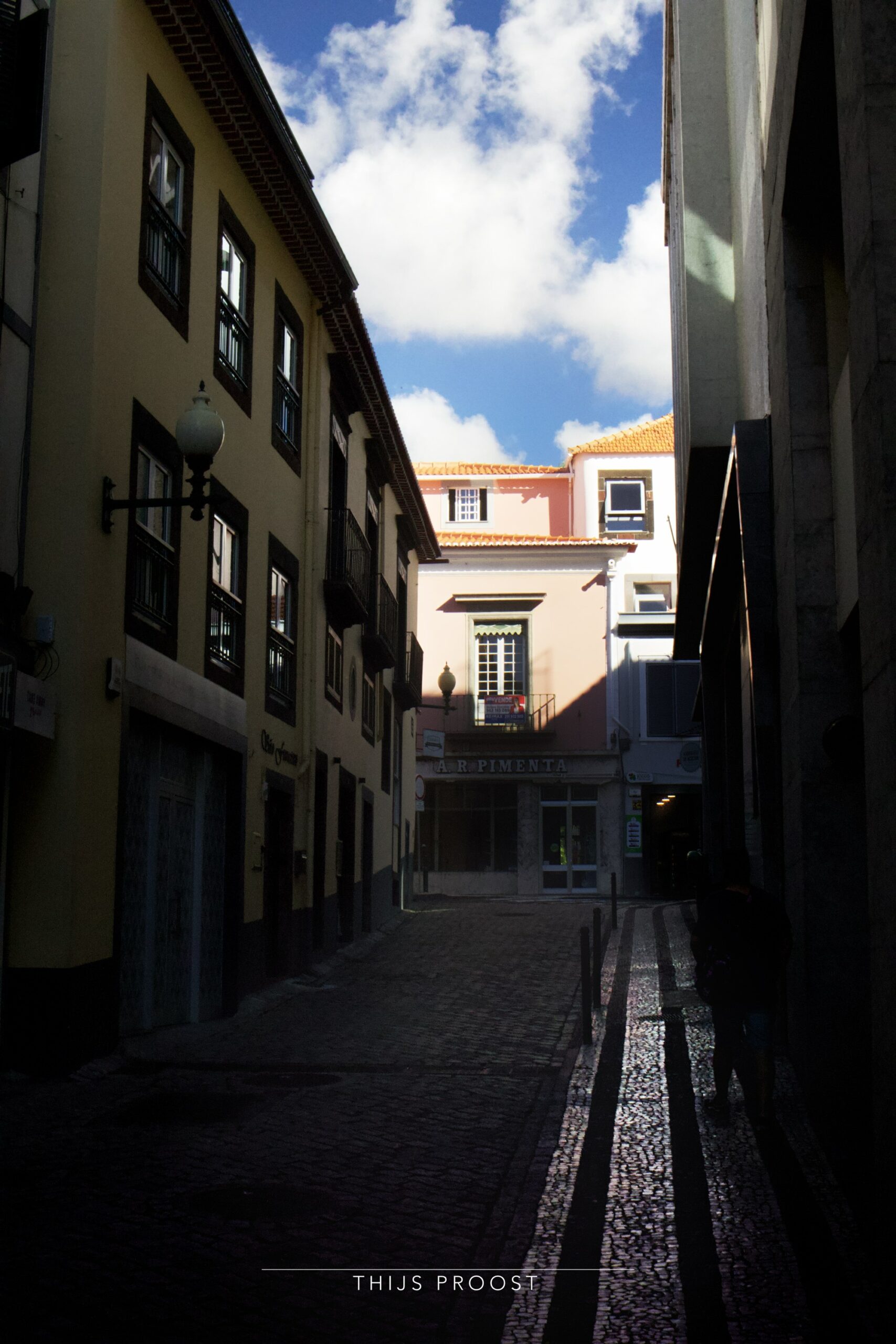 A view of a dark alley in the center of Funchal Madeira. Light falls on the buildings at the end of the alley.