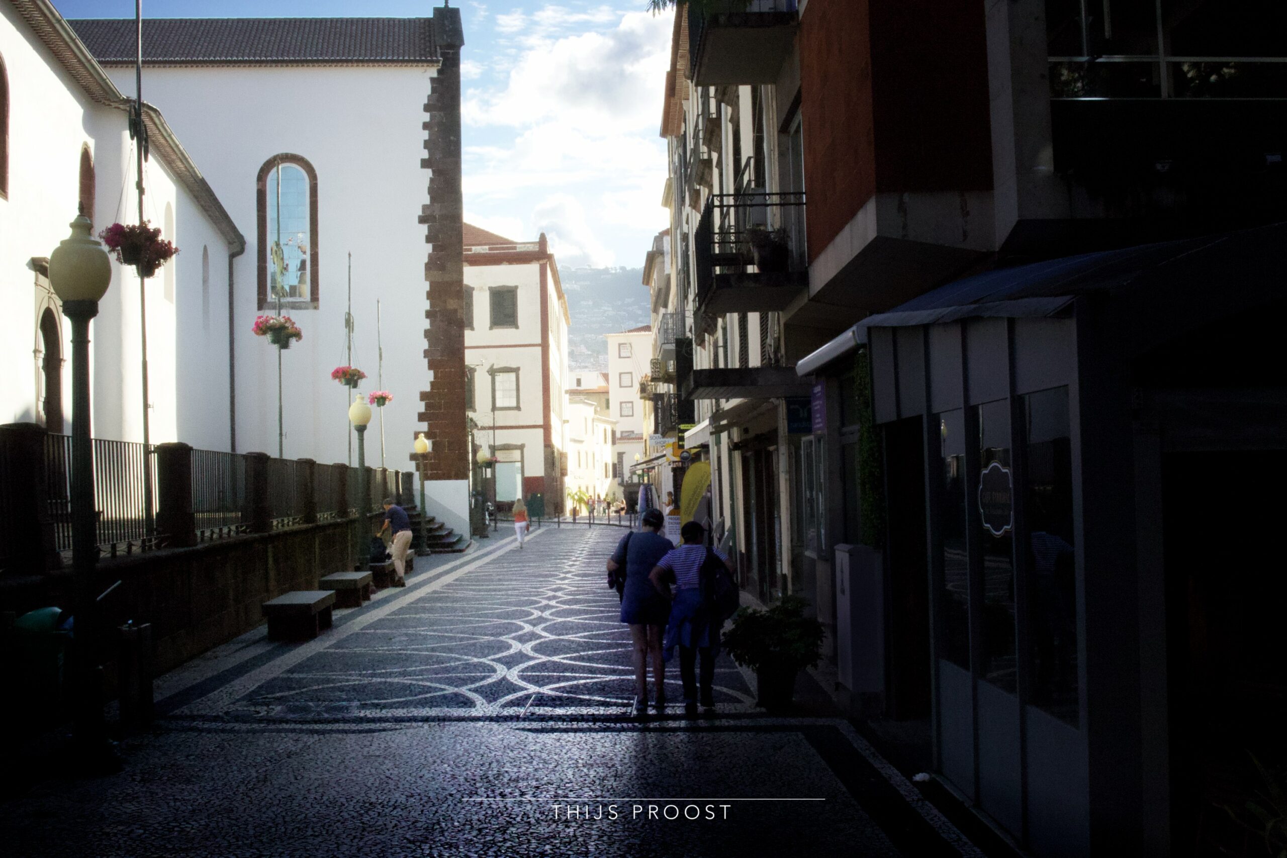 View of a street with a church in the center of Funchal Madeira. The buildings on the right are in the shadow and the church on the left in lightly lit.
