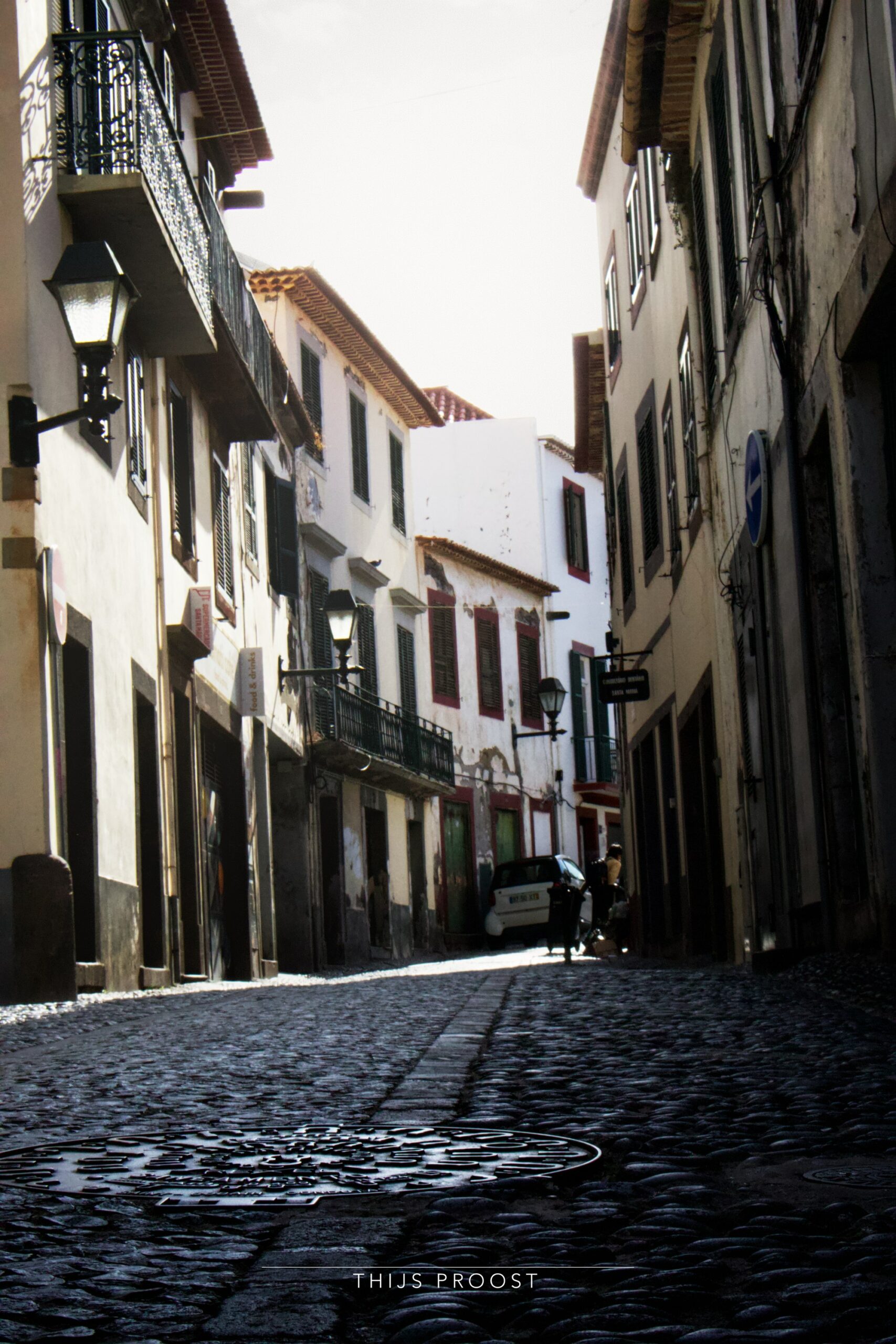 A view of a street in the center of Funchal Madeira. Light hits the buildings while the street remains in shadow.