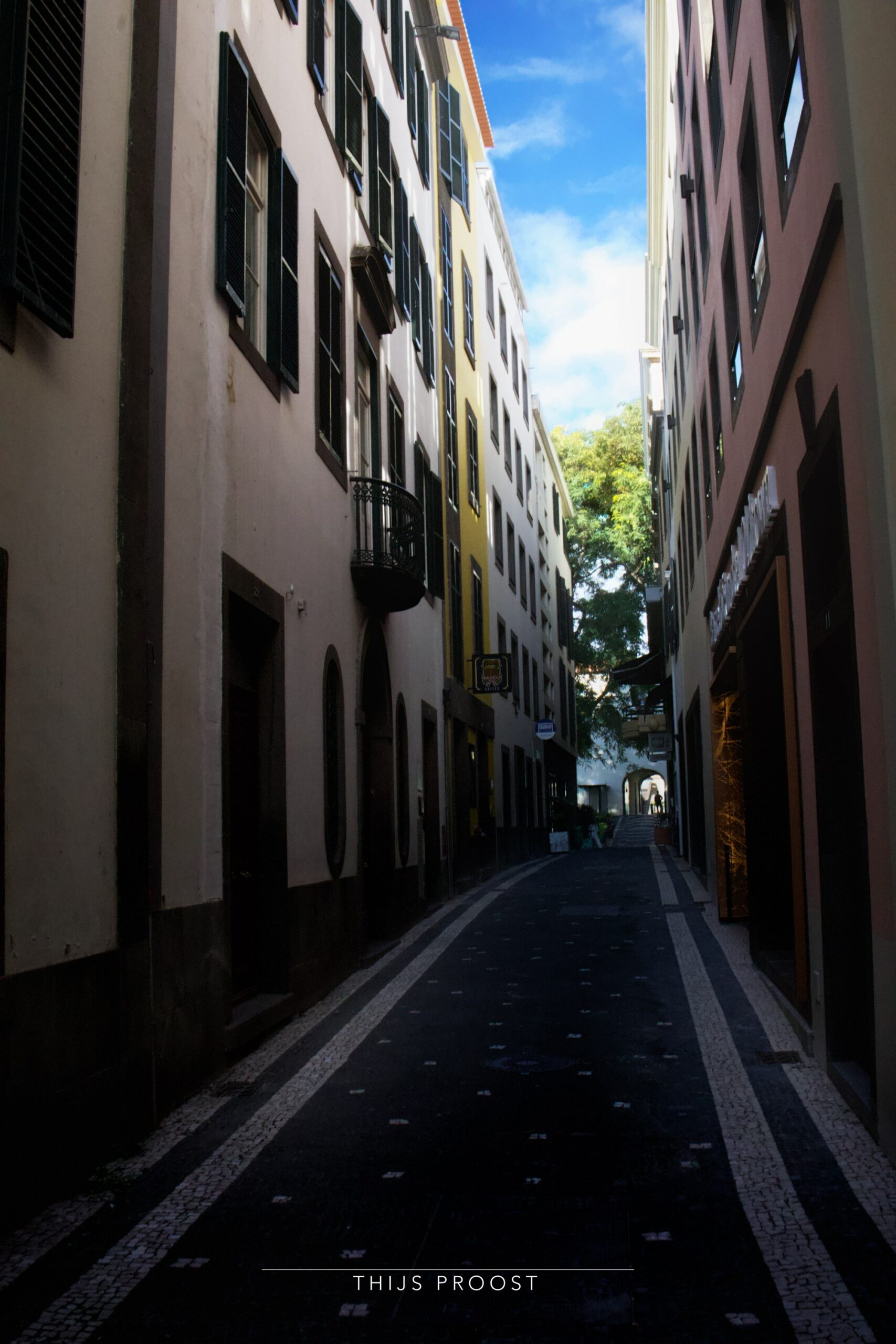 A street in shadow in the center of Funchal Madeira. The sky in the center brakes the two halfs of the image.