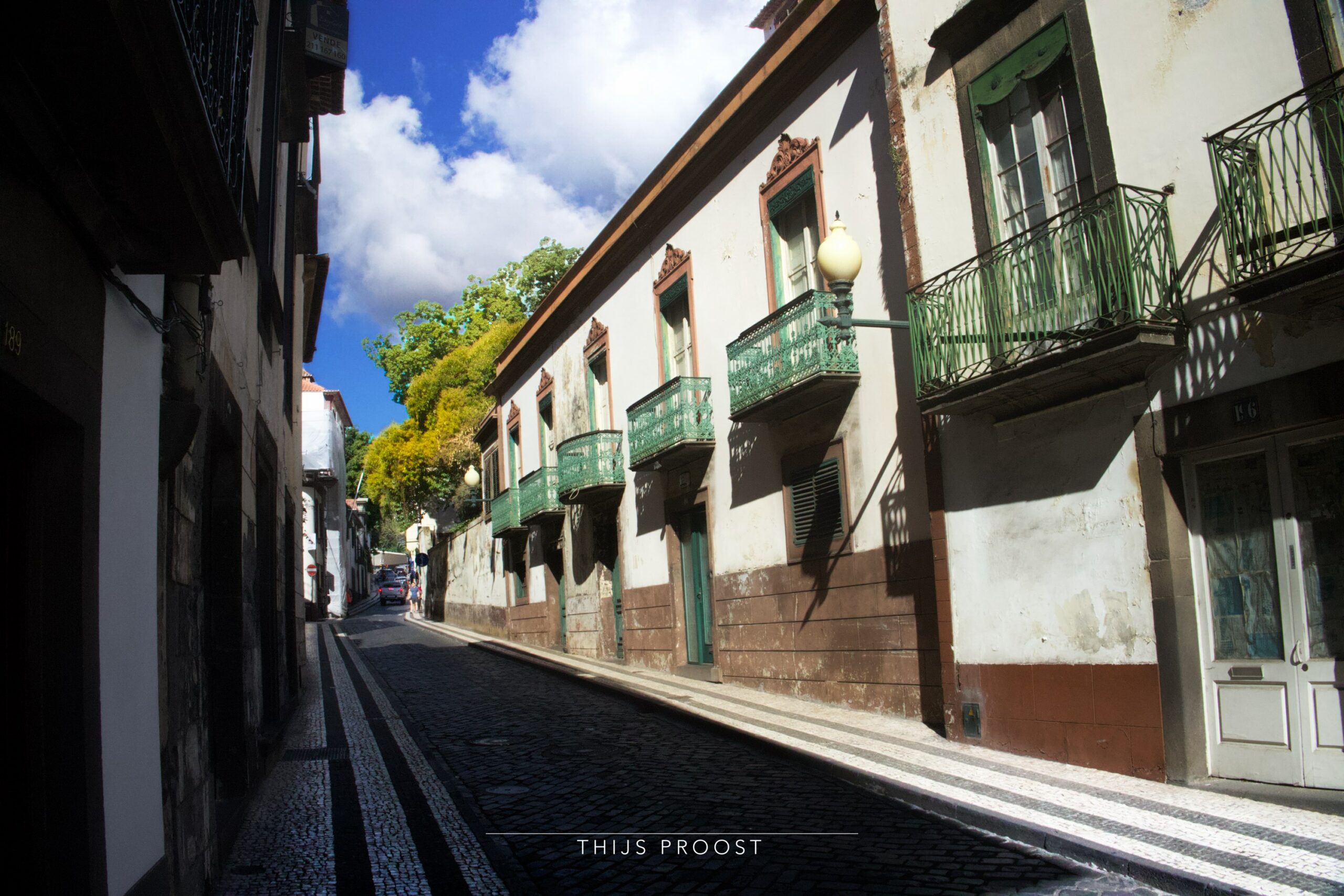 Old street in the center of Funchal. There are balconies at all windows at the building on the right. Clouds are in the sky.
